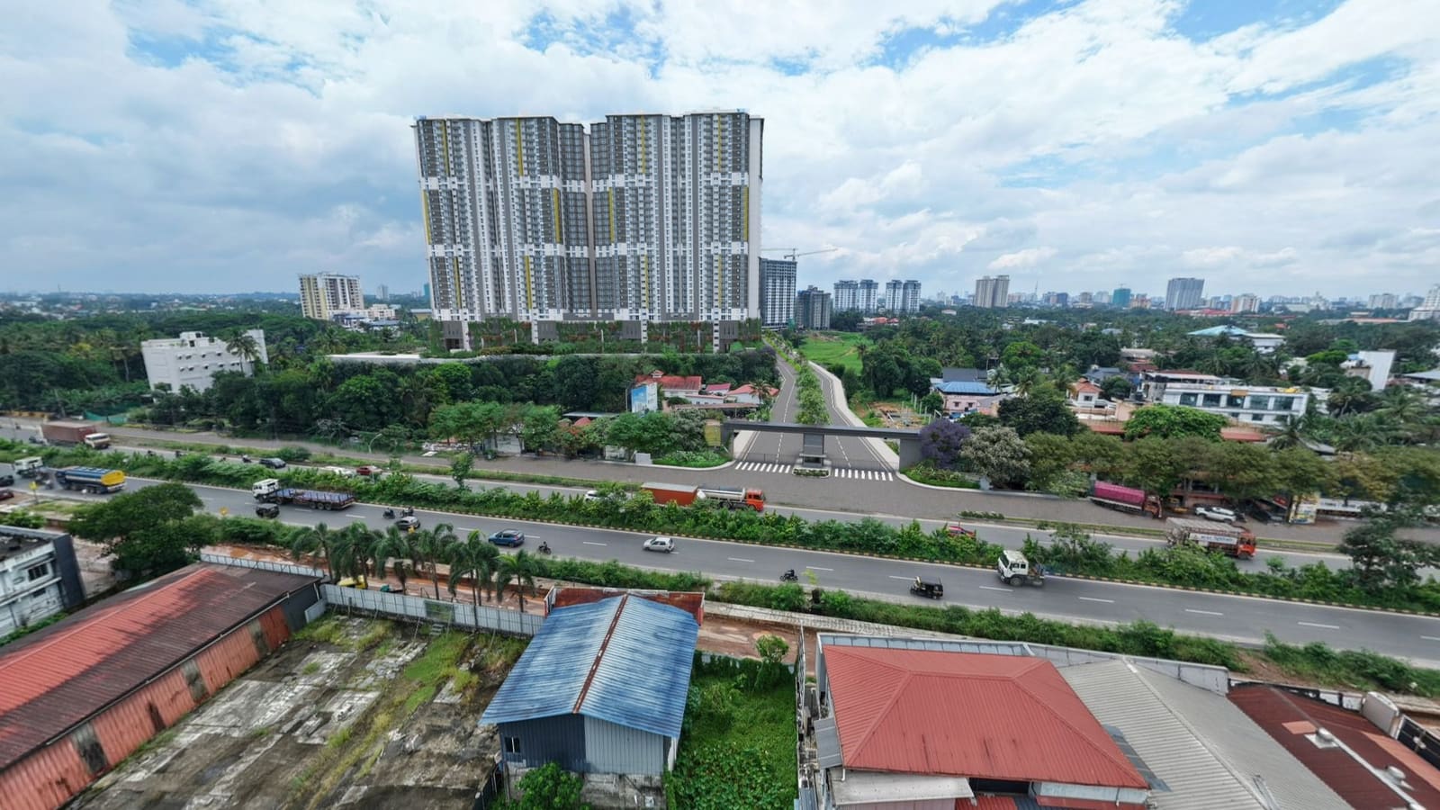 Aerial photograph over Edappally, looking across a highway junction and low-rise rooftops towards high-rise buildings beyond the trees.